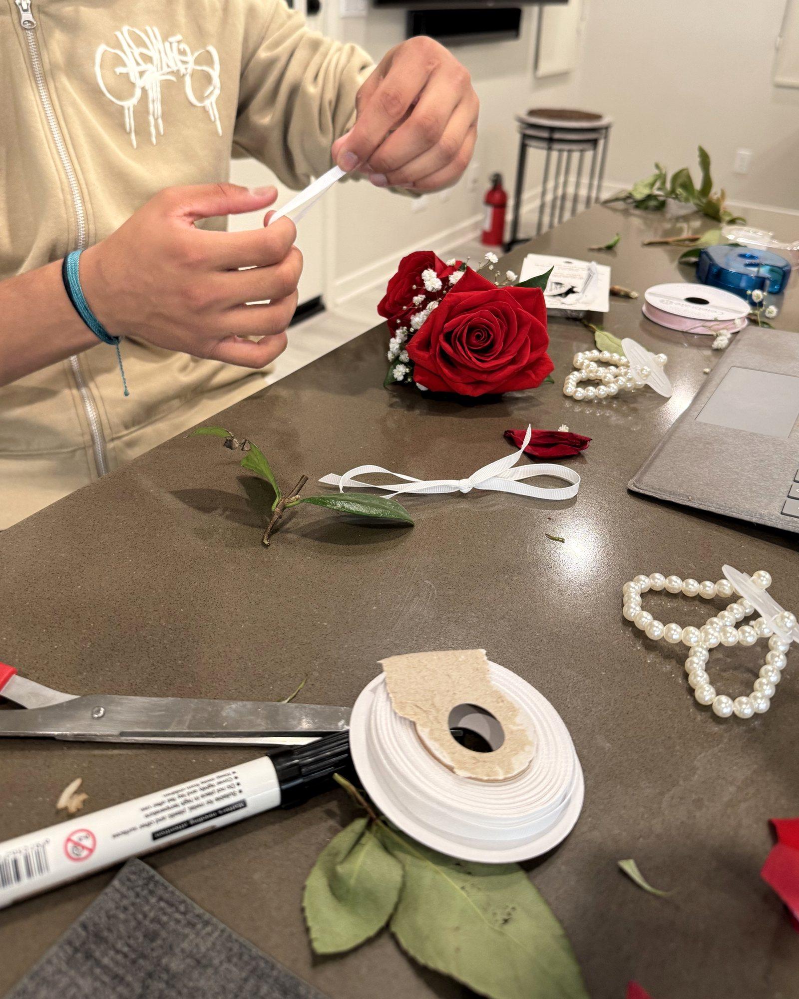 Hands wrapping ribbon at a counter covered in roses, pearls and ribbon